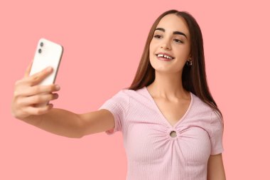 Diastemalı genç bir kadın pembe arka planda selfie çekiyor.