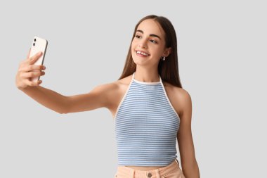 Diastemalı genç bir kadın arka planda selfie çekiyor.