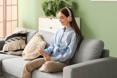 Kulaklık takan, diyabetik hastası genç bir kadın evdeki koltukta cep telefonu kullanıyor.