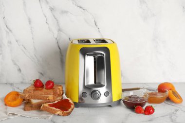 Ekmek dilimleri, kayısılar, çilekler ve reçeller beyaz mermer arka planda.