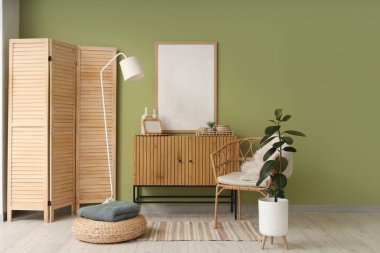 Rahat koltuklu modern odanın içi, katlanan ekran ve boş çerçeve yeşil duvarın yanında.