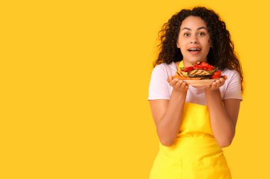 Sarı arka planda bir tabak ızgara sebzeli Afro-Amerikan kadın.