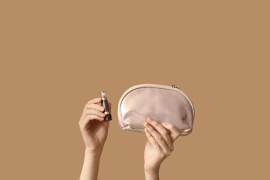 Kozmetik çantalı kadın elleri ve kahverengi arka planda ruj.