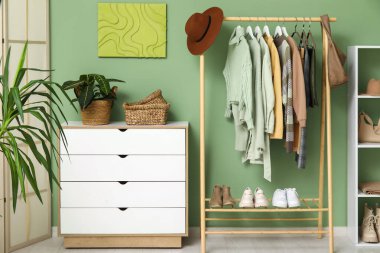 Askıda asılı şık sonbahar giysileri ve yeşil duvara karşı çekmeceler