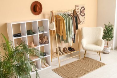 Giysilerle, koltukla ve soyunma odasındaki bej duvarın yanındaki raflarla dolu.