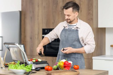 Genç adam lezzetli sebzelere zeytinyağı ekliyor. Mutfaktaki modern elektrikli ızgaraya şiş koyuyor.