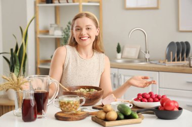 Mutfaktaki masada okroshka pişiren genç bir kadın.
