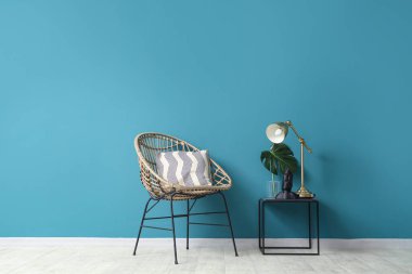 Mavi duvarın yanında heykelcik, canavar yaprağı ve masa lambası olan sandalye ve kahve masası.