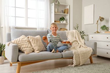 Evdeki kanepede oturan tatlı kekleri olan küçük çocuk.