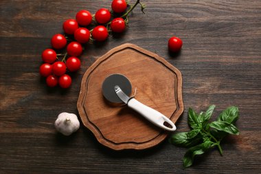 Üzerinde paslanmaz çelik pizza bıçağı, domates ve fesleğen olan bir tahta.