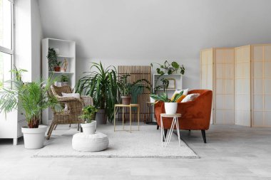 Yeşil çiçekleri, kanepesi ve hasır koltukları olan bir oturma odası.