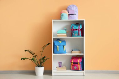 Turuncu duvarın yanında kitap ve sırt çantaları olan raf ünitesi.