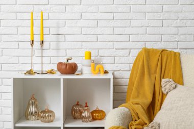 Süslü balkabaklı raf ünitesi ve beyaz tuğla duvarın yanında yanan mumlar.