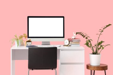 Boş bilgisayar monitörü, çalar saati ve pembe arka planda bitkileri olan modern işyeri