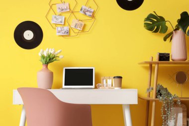 Modern dizüstü bilgisayarı, vinil diskleri ve sarı duvarda asılı ruh hâli tahtası olan şık çalışma alanının içi.