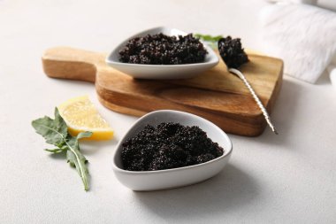 Lezzetli siyah havyar, roka ve beyaz arka planda bir dilim limon.