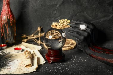 Kristal küreyle kanlı cadı eli, kuru çiçekler ve grunge siyah arka planda sihirli özellikler. Cadılar Bayramı
