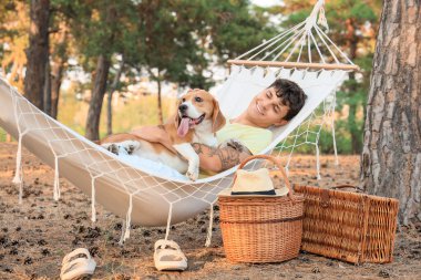 Beagle köpeği olan genç bir adam hamakta yatıyor.
