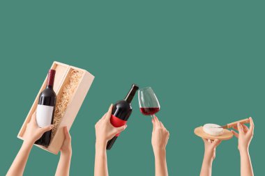 Yeşil arka planda şarap ve peynir şişelerini tutan kadın eller.