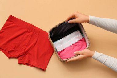 Kadın, katlanmış erkek mayolarını bej arka planda hasır sepete koyuyor.