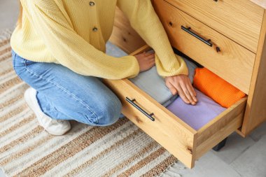 Genç bir kadın evdeki şifoniyere temiz giysiler koyuyor.