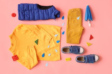 Pembe arka planda şık çocuk kıyafetleri, ayakkabıları, oyuncakları ve kağıt yağmur damlaları olan kompozisyon