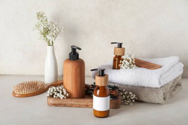 Ahşap tepsiyle kompozisyon, şampuan şişeleri ve bej rengi grunge duvarın yanındaki masada çiçekler.