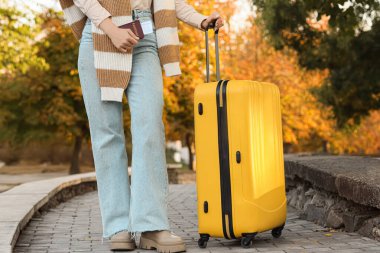 Sonbahar parkında bavulu ve pasaportu olan kadın, yakın plan.