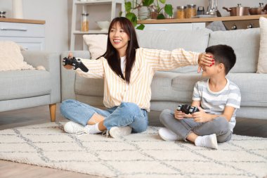 Genç anne ve küçük oğlu evde yerde video oyunu oynuyorlar.