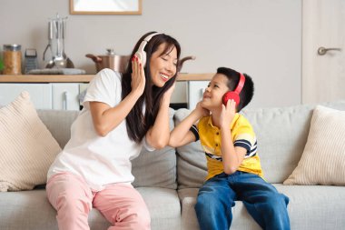 Genç anne ve küçük oğlu modern kulaklıklarıyla evde müzik dinliyorlar.