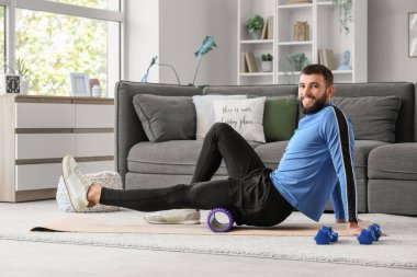 Evde yoga minderinde köpükle egzersiz yapan genç bir adam.