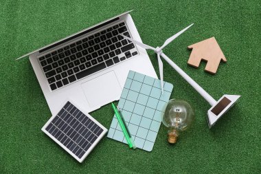 Güneş panelli dizüstü bilgisayar, rüzgar türbini, ampul ve çimlerin üzerinde ev figürü. Yeşil Enerji kavramı
