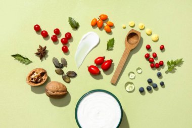 Yeşil zemin üzerinde doğal krema kavanozu ve farklı malzemelerle kompozisyon