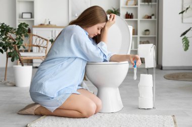 Hamile olan genç bir kadın tuvalette klozetin yanında oturuyor.