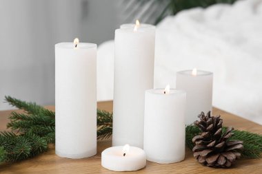 Farklı yanan mumlar, çam kozalakları ve ahşap masada köknar dalları.