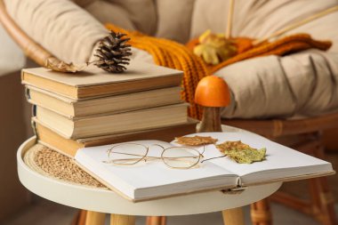 Oturma odasında kitap, gözlük ve sonbahar süslemeleri olan sehpa, yakın plan.