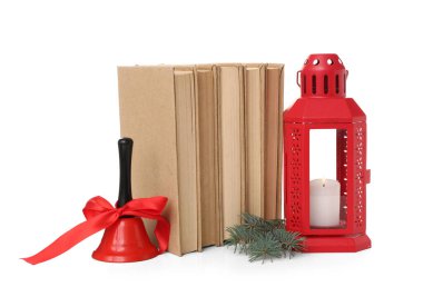 Kitap seti, yanan mum fener ve beyaz arka planda Noel çanı.