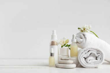 Kozmetik ürünleri, spa taşları, temiz havlular ve açık ahşap masadaki çiçekler.