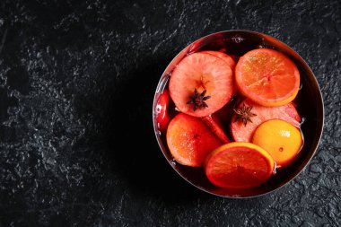 Siyah arka planda elma ve portakallı sıcak sıcak şarap pişirmek.