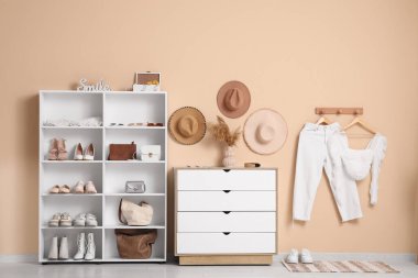 Farklı kadın ayakkabıları, aksesuarları, çekmeceleri ve renkli duvarda asılı giysileri olan raf ünitesi.