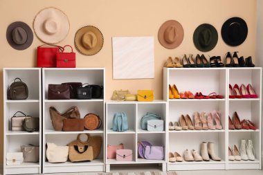 Renkli duvarda farklı kadın ayakkabıları, el çantaları ve şapkaları asılı raf ünitesi.