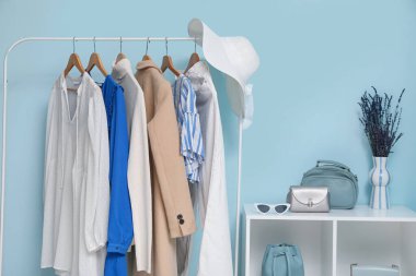 Askıda asılı şık kadın kıyafetleri ve renkli duvarların yanında aksesuarlar.