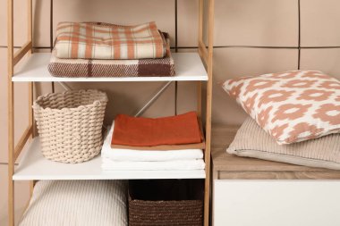 Odadaki bej fayans duvarının yakınındaki raflarda temiz çarşaf ve sepet var.