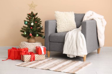 Koltuk ve küçük Noel ağacı. Odada bej duvarın yanında hediyeler var.