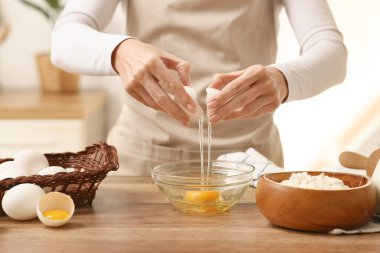 Kadın mutfak tezgahında hamur hazırlamak için yumurtayı kaseye kırıyor.