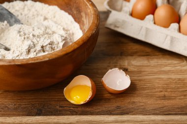 Ahşap zemin üzerinde hamur hazırlamak için kırık yumurta ile bir kase un.