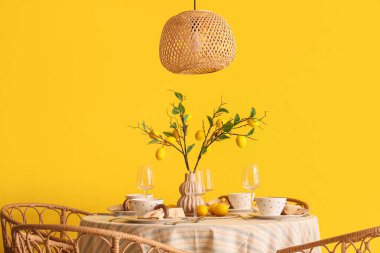 Yemek odasındaki sarı duvarın yanında güzel limon dallarıyla süslenmiş şık bir masa.