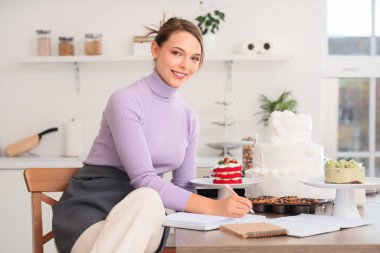 Mutfaktaki deftere pasta yazan kadın pastacı.