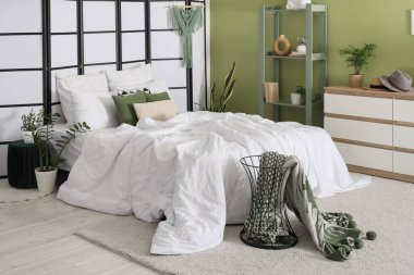 Yatak odasının içinde raf ünitesi, çekmece ve yeşil bitkiler var.