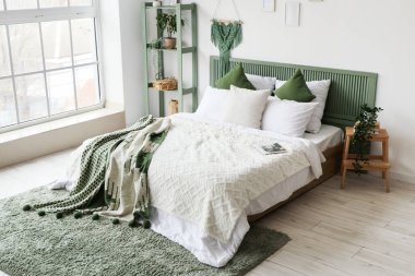 Yatak odasının içinde yeşil ekose ve raf ünitesi olan modern bir yatak.